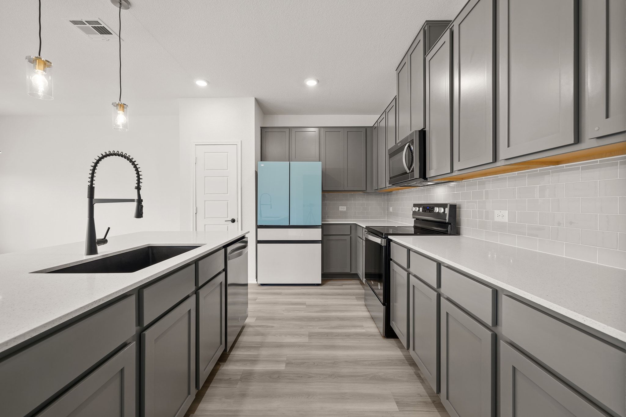 7715 Libretto Lane Austin, TX 78744 - Photo 10 of 39 The kitchen centers around a large island with breakfast bar seating and includes quartz countertops, tall cabinetry, subway tile backsplash, and modern appliances (all included).