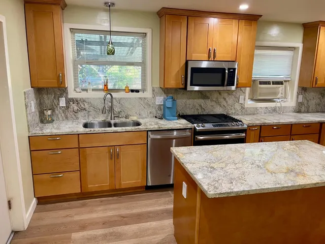 a kitchen with stainless steel appliances granite countertop a sink a stove a microwave and wooden cabinets