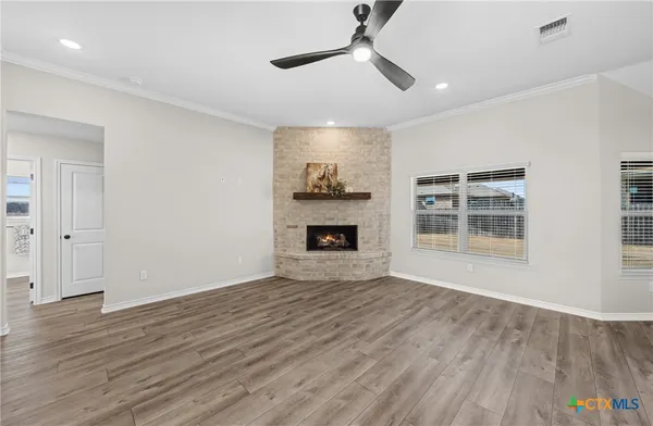 a view of a livingroom with wooden floor a ceiling fan a fireplace and windows