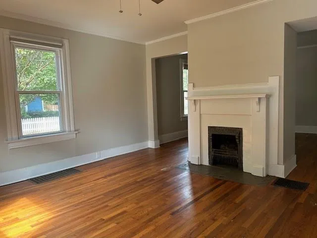 a view of an empty room with wooden floor fireplace and a window