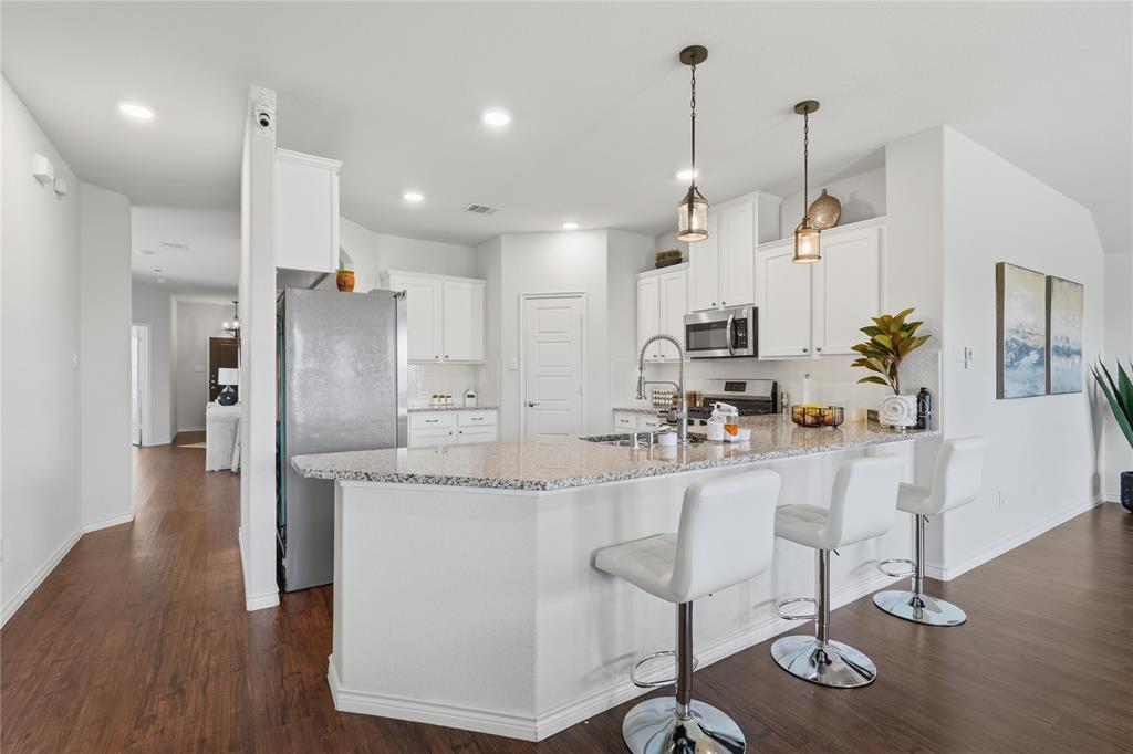 10101 Travis Road Little Elm, TX 75068 - Photo 14 of 26 a kitchen with stainless steel appliances kitchen island granite countertop a refrigerator a stove a sink a dining table and chairs with wooden floor