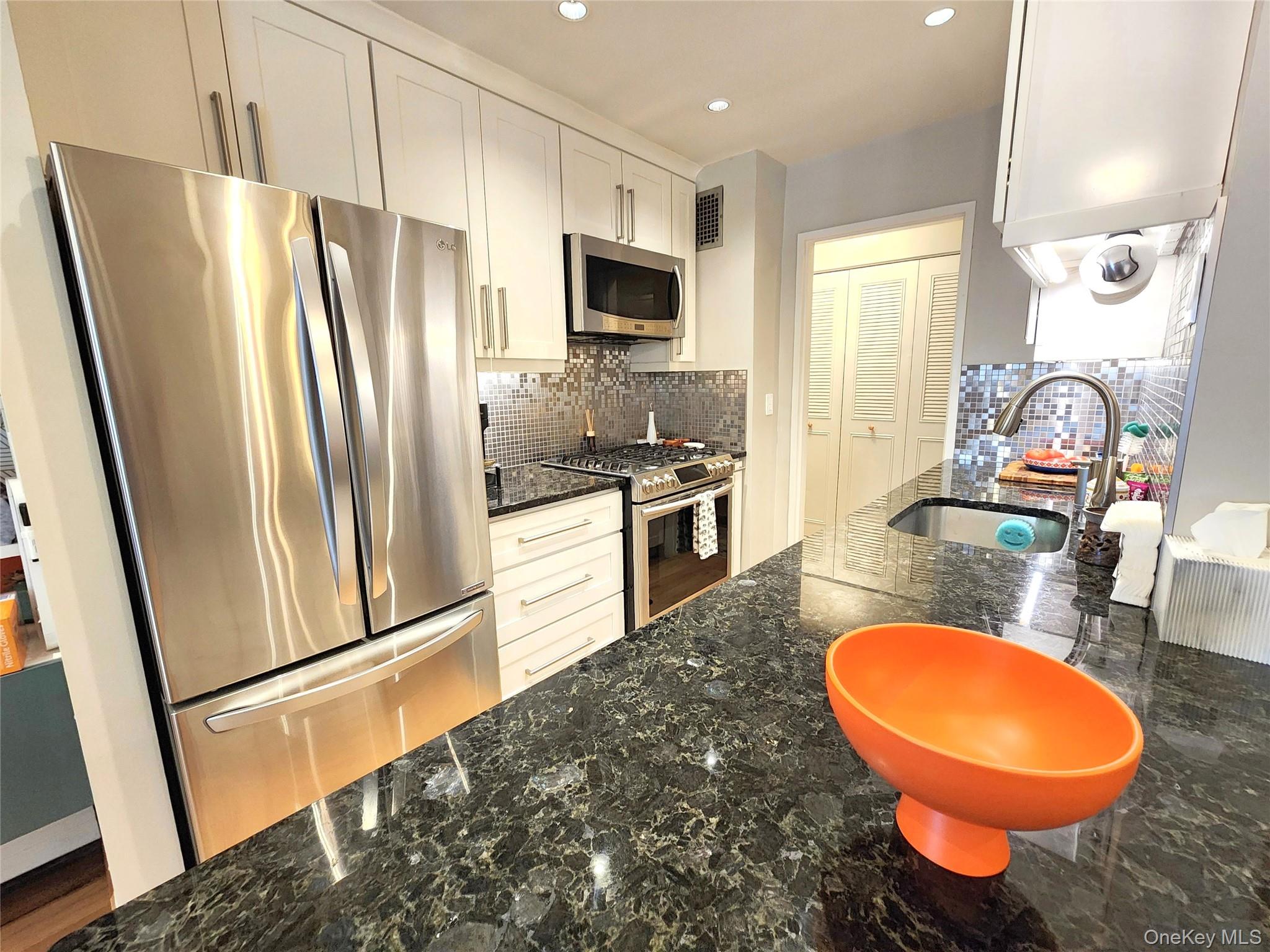25 Park Place, Unit 3R Great Neck, NY 11021 - Photo 3 of 18 a kitchen with stainless steel appliances granite countertop a refrigerator a stove a sink a microwave a dining table and chairs