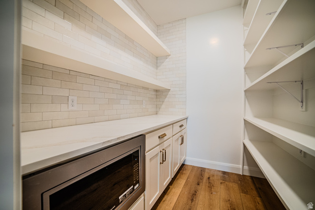 223 South Cottonwood Road, Unit 7501 Vineyard, UT 84059 - Photo 39 of 45 Kitchen pantry featuring a built-in microwave, white shaker cabinetry with brass hardware, open shelving, and wood-finish flooring