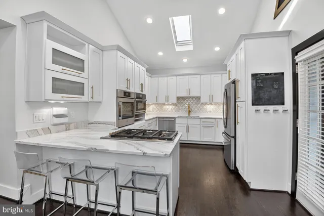 a kitchen with stainless steel appliances a stove a refrigerator a sink and white cabinets with wooden floor