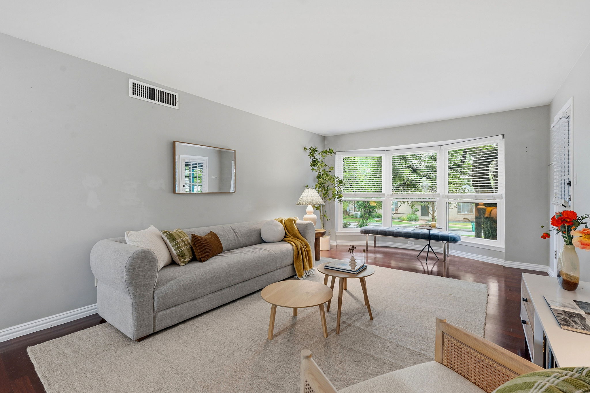 A well-lit living space features rich hardwood flooring and a large bay window, inviting ample natural light.