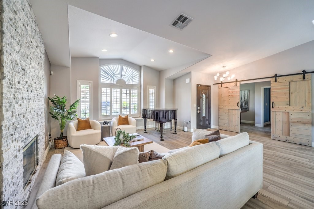 2432 Ocean Front Drive Las Vegas, NV 89128 - Photo 7 of 53 Living area with vaulted ceiling, a barn door, a chandelier, wood finished floors, and a stone fireplace