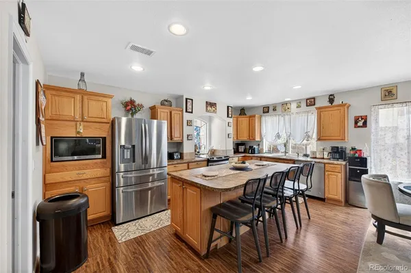 a kitchen with stainless steel appliances granite countertop a refrigerator a stove a sink a dining table and chairs with wooden floor
