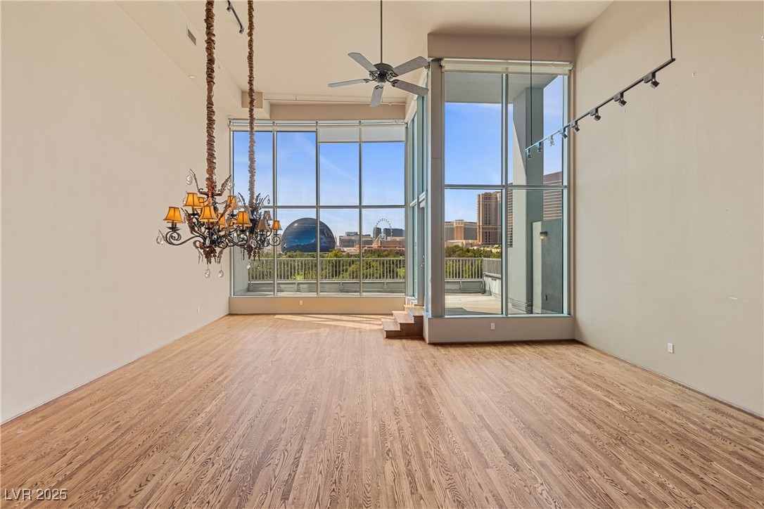 360 East Desert Inn Road, Unit 605 Las Vegas, NV 89109 - Photo 12 of 43 Unfurnished living room with wood finished floors, a chandelier, a ceiling fan, a towering ceiling, and a view of city