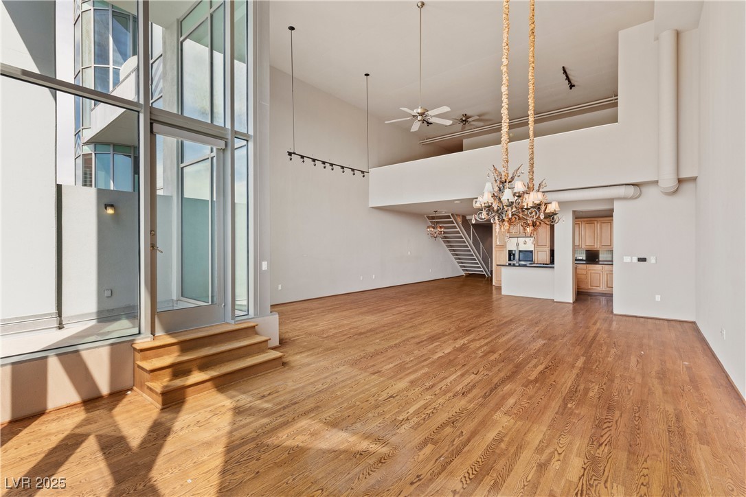 360 East Desert Inn Road, Unit 605 Las Vegas, NV 89109 - Photo 16 of 43 Unfurnished living room featuring stairway, a ceiling fan, light wood finished floors, a high ceiling, and a chandelier