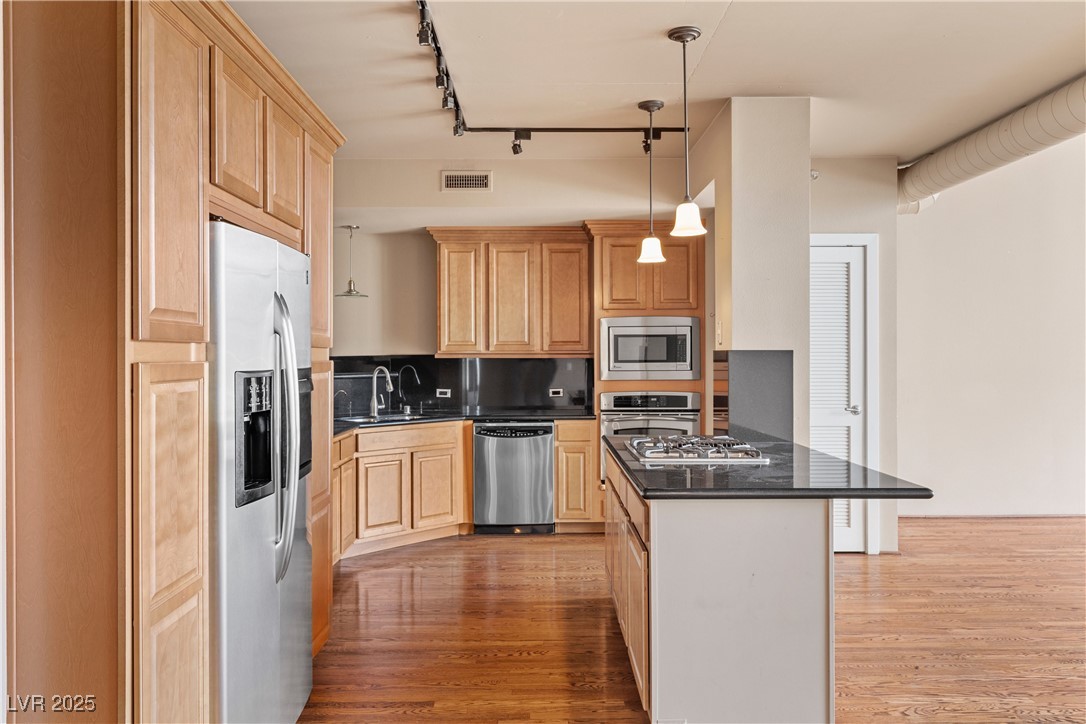 360 East Desert Inn Road, Unit 605 Las Vegas, NV 89109 - Photo 18 of 43 Kitchen with rail lighting, stainless steel appliances, decorative light fixtures, dark wood-style flooring, and dark stone countertops