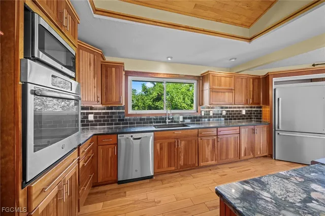 a kitchen with stainless steel appliances granite countertop a refrigerator a sink dishwasher a stove and white countertops with wooden floor