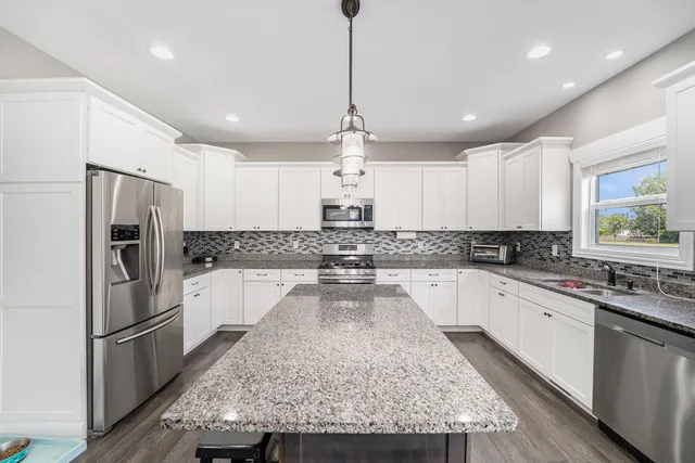 a large kitchen with kitchen island a stove a refrigerator a sink dishwasher a oven with white cabinets and wooden floor