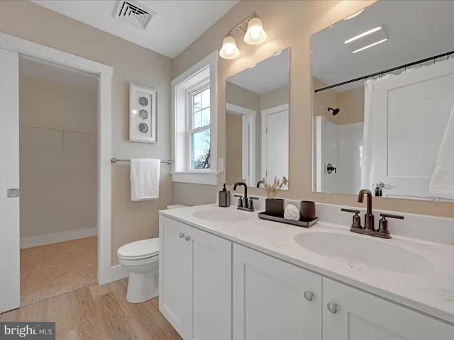 a bathroom with double vanity sinks a toilet a mirror and shower