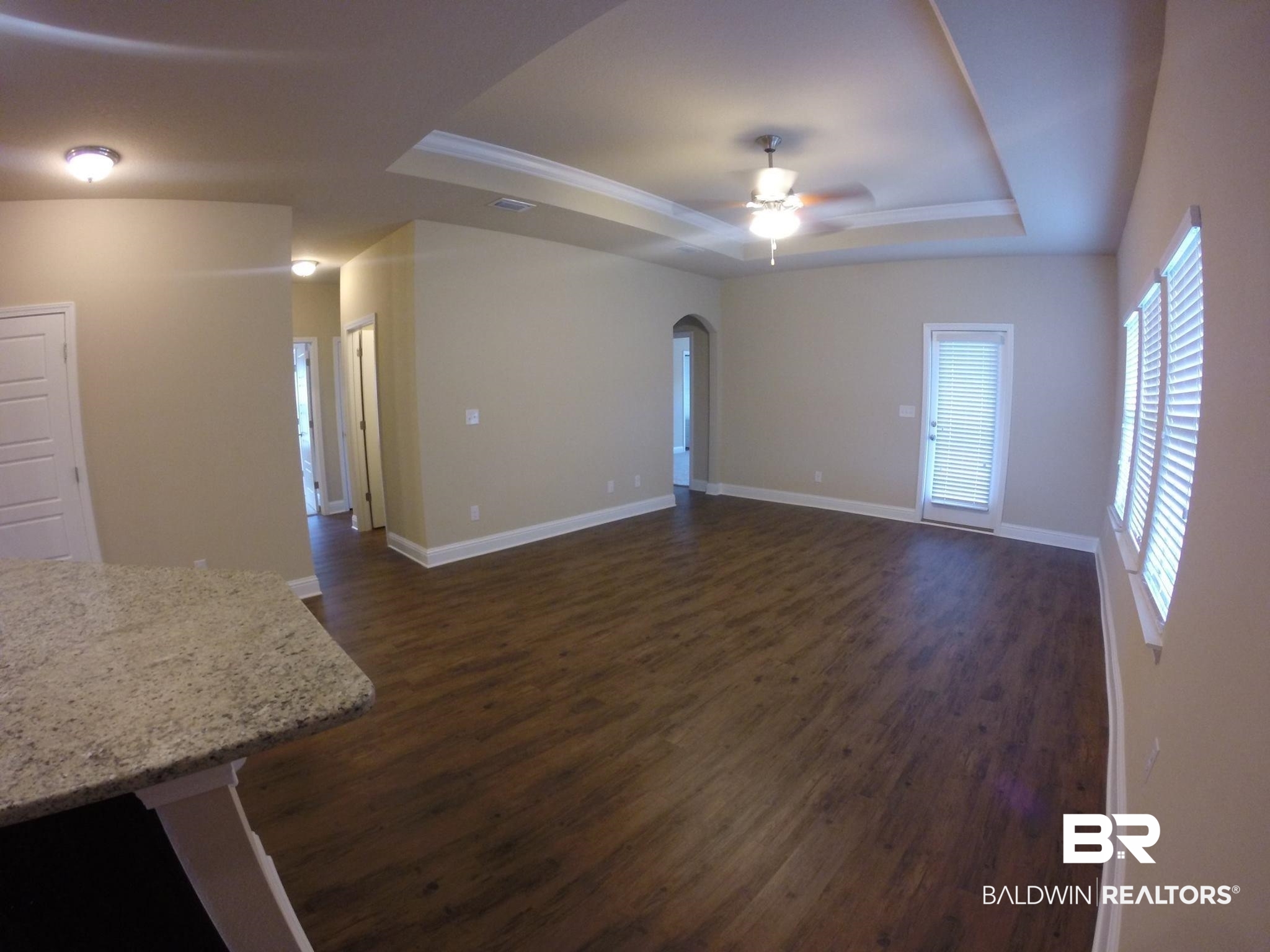 2996 Notsram Court Mobile, AL 36695 - Photo 4 of 16 Unfurnished living room featuring dark wood-style floors, a ceiling fan, baseboards, and a tray ceiling