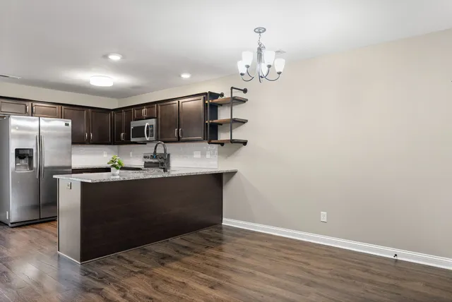 a kitchen with stainless steel appliances granite countertop a refrigerator a sink dishwasher a stove and a dining table with wooden floor