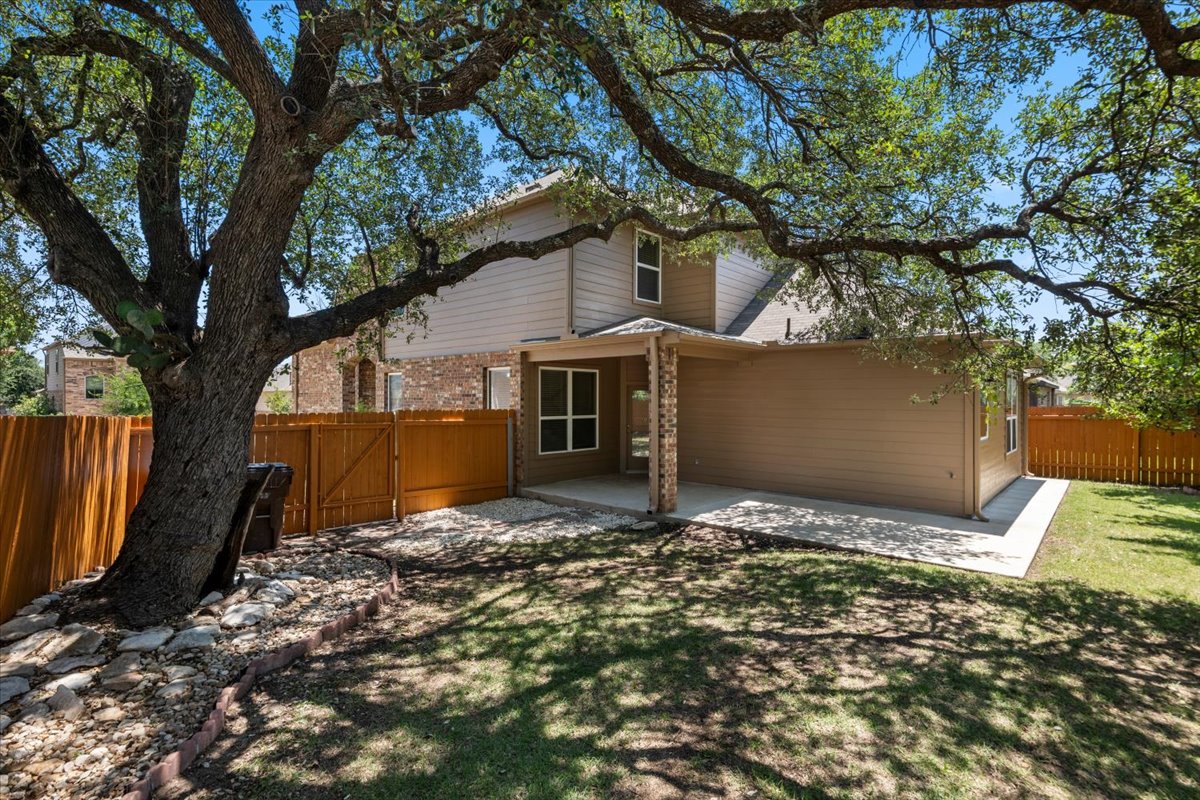 3451 Mayfield Ranch Boulevard, Unit 311 Round Rock, TX 78681 - Photo 38 of 40 Expansive backyard featuring a mature shade tree, a covered patio with brick columns, an extended concrete patio, a manicured lawn, and a wooden privacy fence
