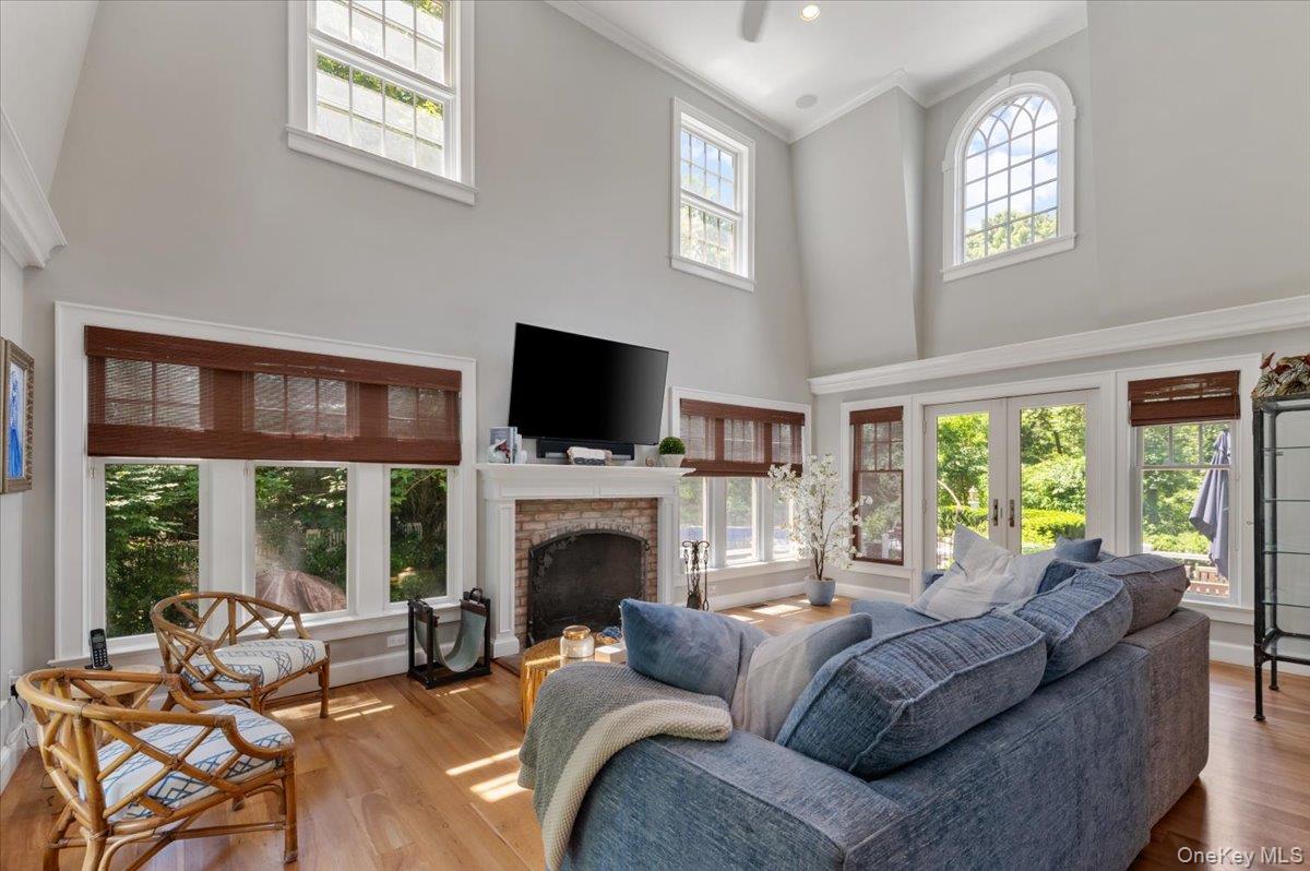 5 Fox Hunt Court Cold Spring Harbor, NY 11724 - Photo 6 of 42 Living area featuring a brick-surround fireplace, hardwood flooring, and multiple large windows with custom shades