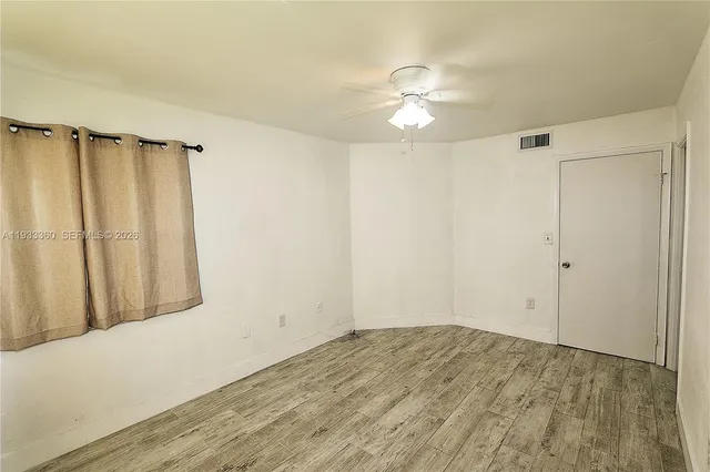 an empty room with wooden floor fan and windows