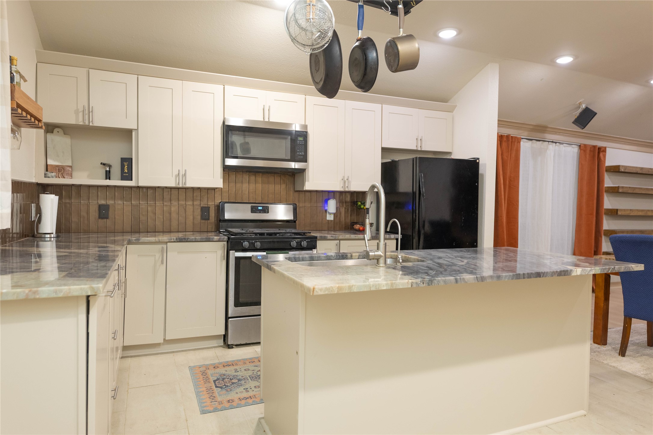 8007 Capitol Street Houston, TX 77012 - Photo 13 of 25 This kitchen features modern cabinetry, stainless steel appliances, and a central island with a marble countertop. It includes a hanging pot rack, tiled backsplash, and ample lighting, creating a bright and functional space.