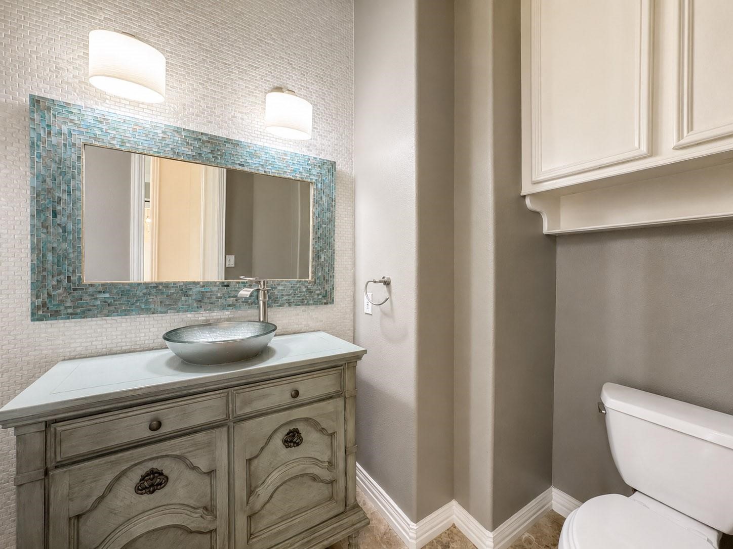 1810 Woerner Road Houston, TX 77090 - Photo 19 of 39 This bathroom features a stylish vanity with a vessel sink and elegant cabinetry. It has a large framed mirror, modern lighting, and a neutral color palette, offering a clean and sophisticated look.