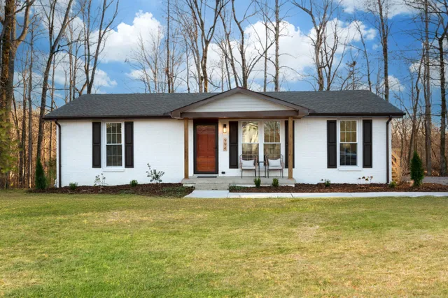 a view of a white house with a large pool and lawn chairs under an umbrella