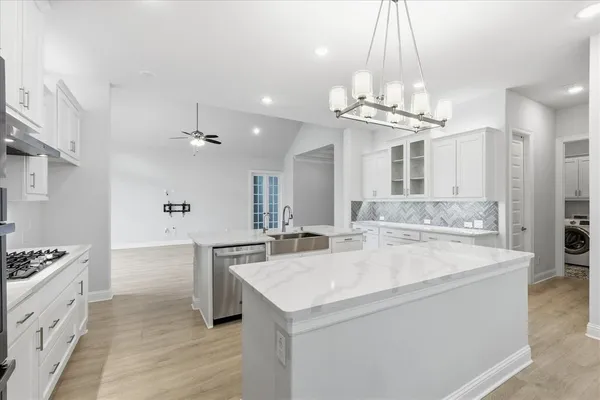 a large white kitchen with a stove a sink a refrigerator and a chandelier