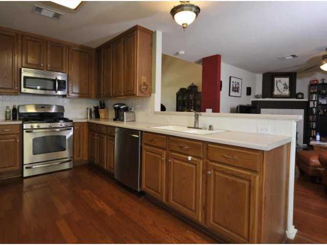 8121 Siringo Pass Austin, TX 78749 - Photo 4 of 9 Kitchen with stainless steel appliances, light countertops, dark wood-type flooring, and wood finish cabinets