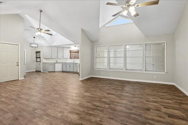 an empty room with wooden floor chandelier fan and windows