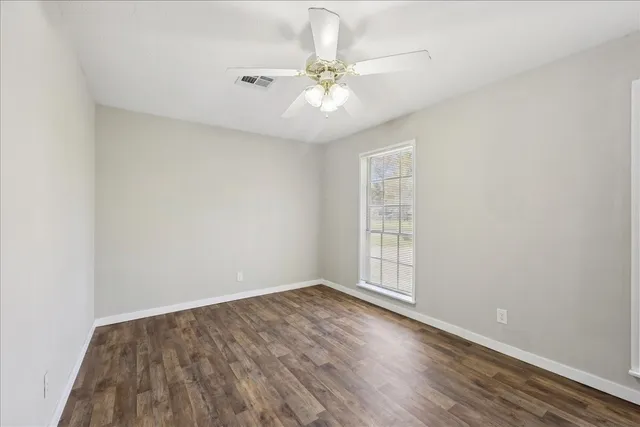 an empty room with wooden floor fan and windows