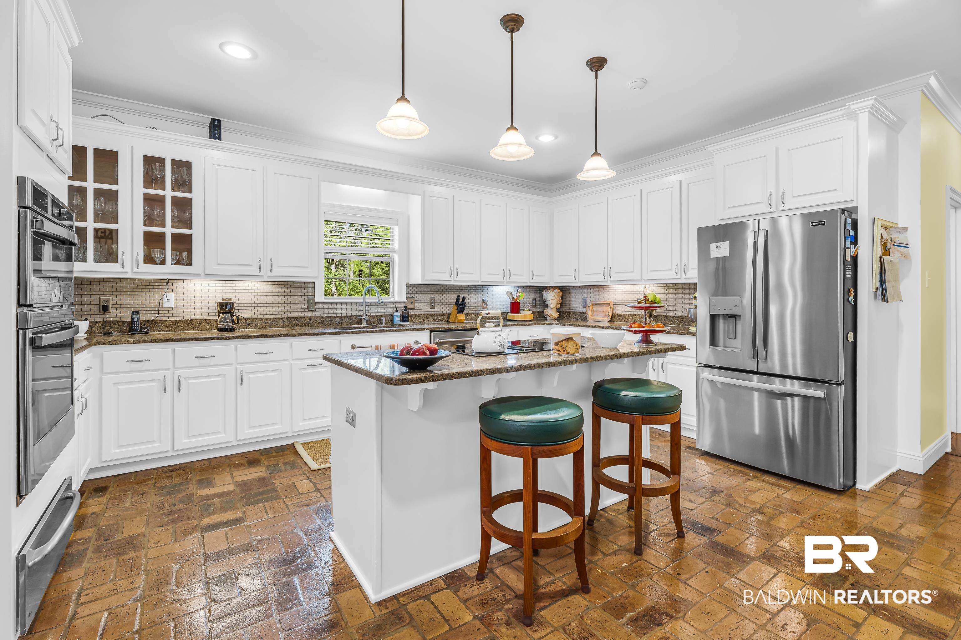 7014 Blakeley Road Daphne, AL 36527 - Photo 28 of 45 Kitchen featuring an eat-at island with a stone countertop, extensive white cabinetry, stainless steel appliances, brick-finish flooring, and pendant lighting