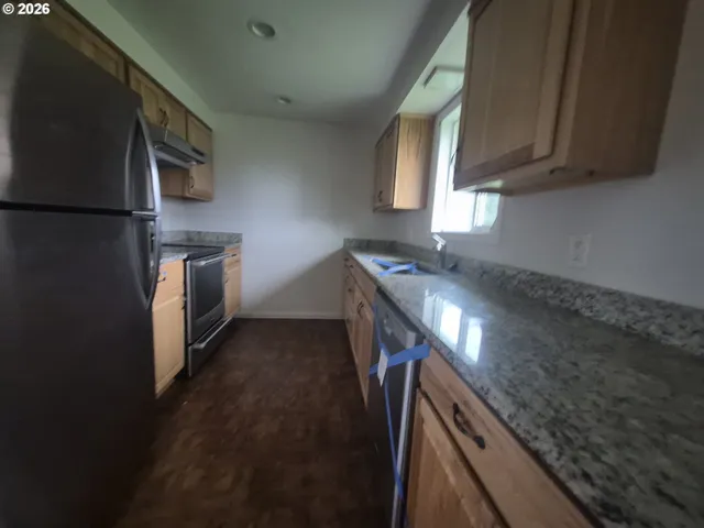 a kitchen with stainless steel appliances granite countertop a refrigerator a stove and a sink with wooden cabinets