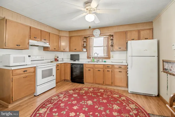 a kitchen with a white refrigerator oven a sink dishwasher and white countertops with wooden floor