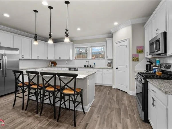 a kitchen with stainless steel appliances granite countertop a stove a sink a refrigerator a microwave a island and chairs with wooden floor