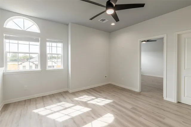 an empty room with wooden floor fan and windows