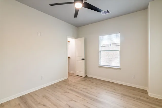 an empty room with wooden floor chandelier fan and windows