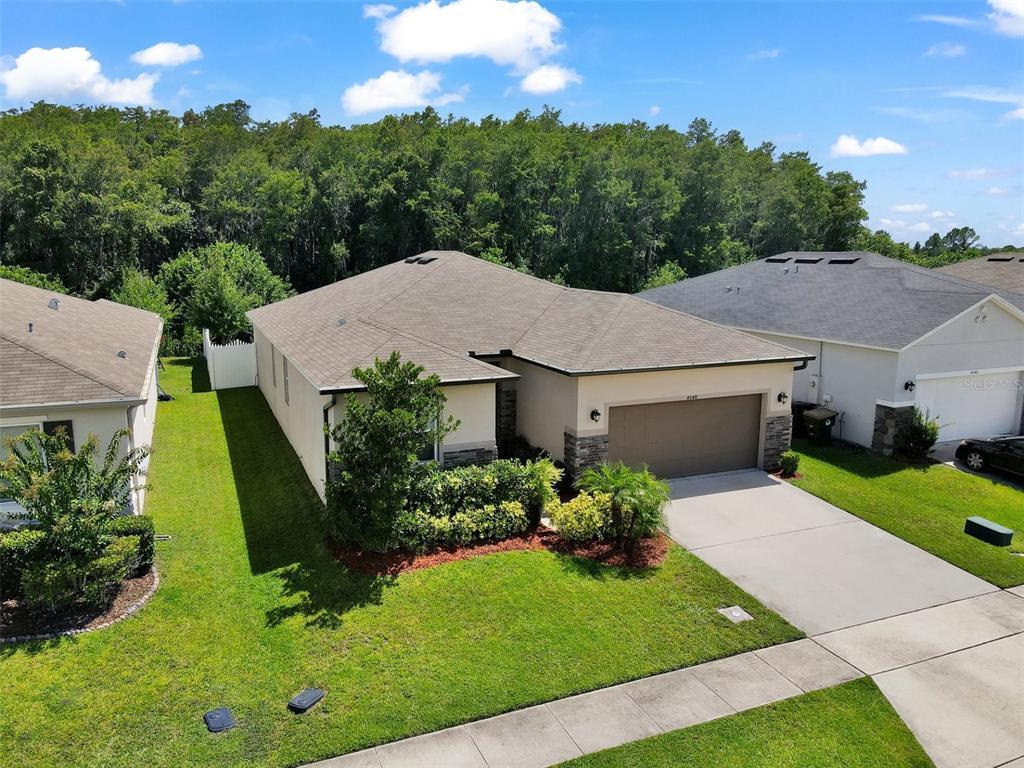 an aerial view of a house with yard and trees in the background