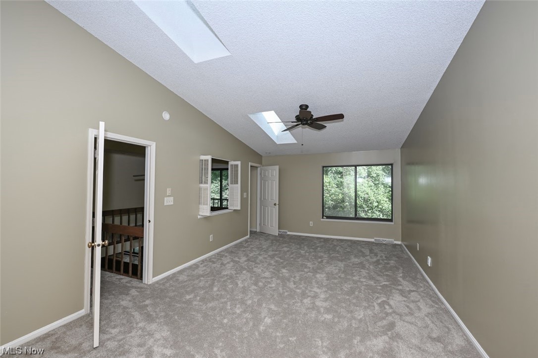 646 Hampton Ridge Drive Akron, OH 44313 - Photo 20 of 33 Empty room featuring a textured ceiling, light carpet, lofted ceiling with skylight, and ceiling fan