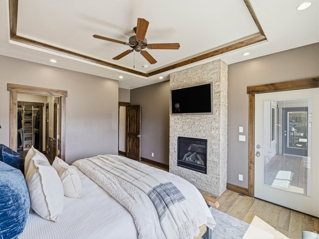 402 Shadow Hill Road Wanship, UT 84017 - Photo 25 of 90 Bedroom featuring a raised ceiling, light wood-style floors, ceiling fan, recessed lighting, and a stone fireplace