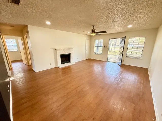 an empty room with wooden floor fireplace and windows