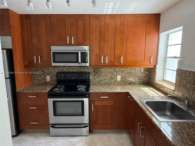 a kitchen with granite countertop wood cabinets stainless steel appliances and a window