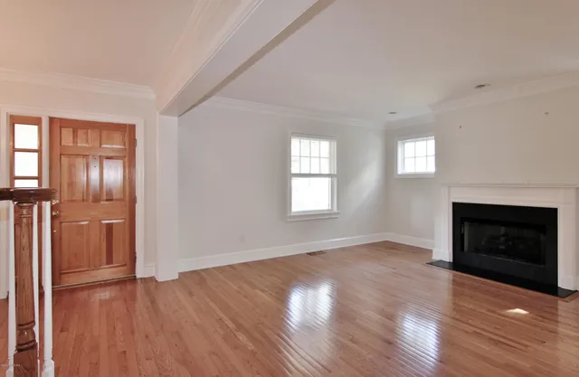 an empty room with wooden floor fireplace and windows