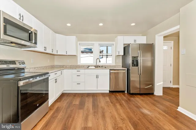 a kitchen with stainless steel appliances granite countertop a refrigerator a stove top oven a sink dishwasher and white cabinets with wooden floor