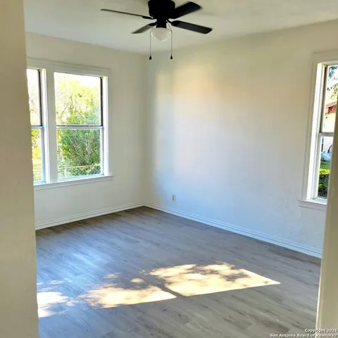 an empty room with wooden floor fan and windows