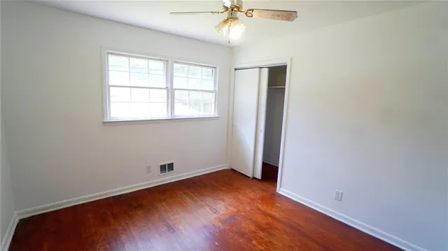 an empty room with wooden floor chandelier fan and windows