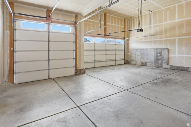 3636 West 910 South Syracuse, UT 84075 - Photo 57 of 70 Spacious two-car garage featuring segmented white doors with upper window panels, concrete flooring, and an exposed concrete foundation wall