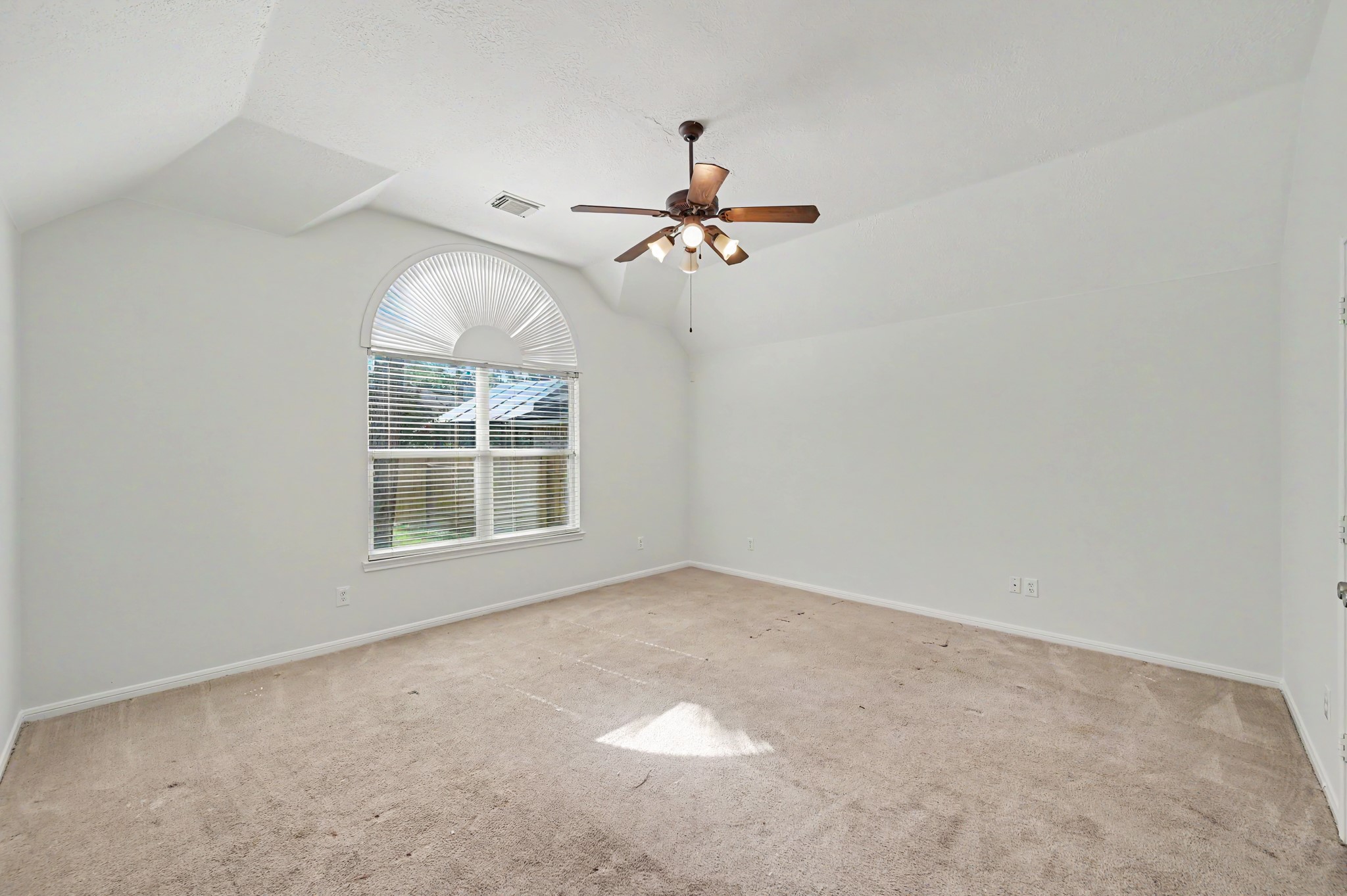 14 South Rambling Ridge Place The Woodlands, TX 77385 - Photo 20 of 42 Spacious primary suite features a vaulted ceiling, elegant arched window, abundant natural light, and plenty of room for a sitting area or oversized furnishings, creating a relaxing private retreat.