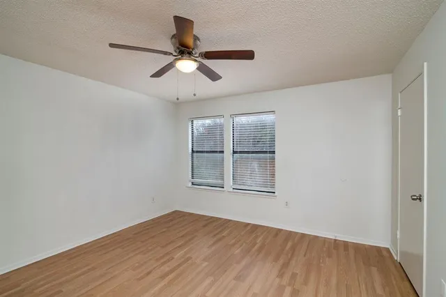 an empty room with wooden floor fan and windows