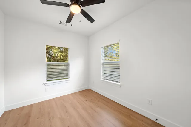 a view of empty room with wooden floor and fan