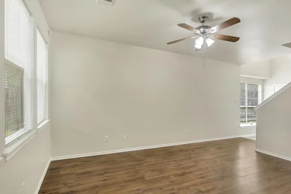 a view of an empty room with wooden floor and a chandelier fan