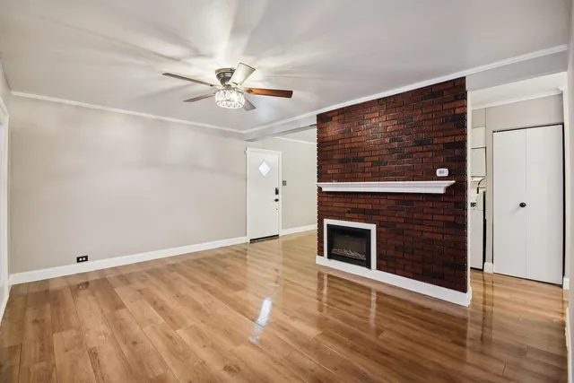 an empty room with wooden floor a ceiling fan a fireplace and windows